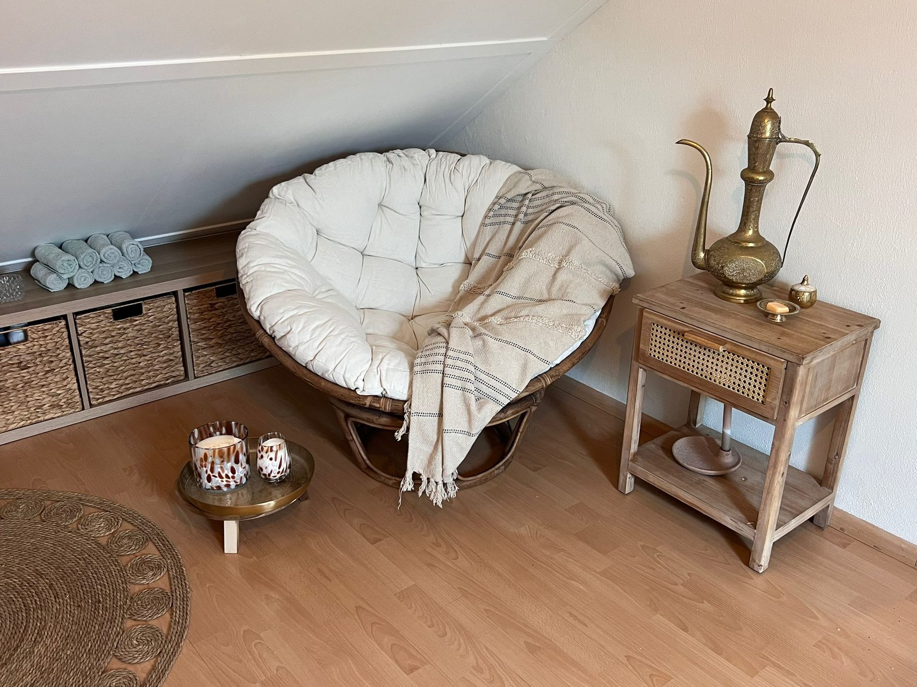 De rustige hoek met een rotan fauteuil, kaarsjes en een koperen kan op een houten tafeltje